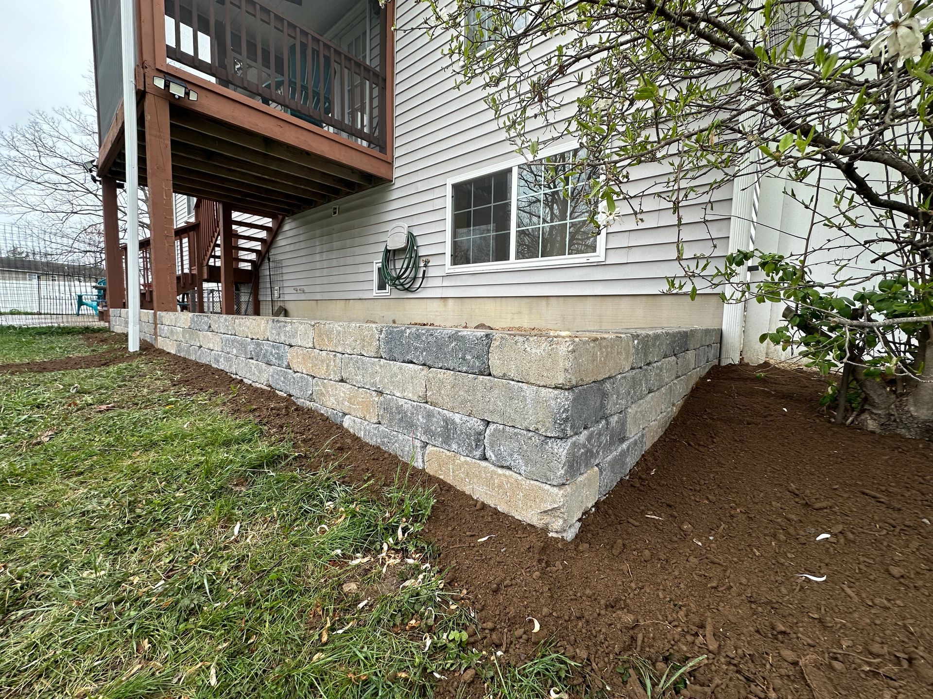A house with a deck and a stone wall in front of it.