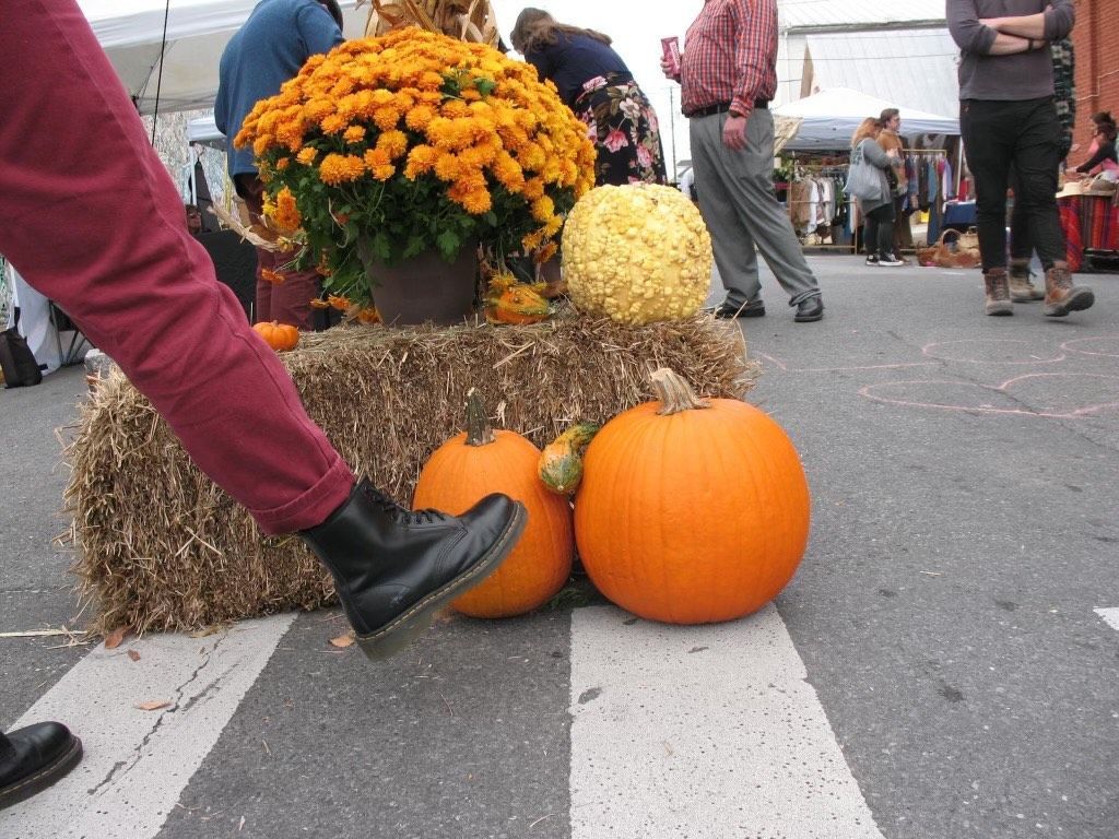 A person 's foot is on a bale of hay next to pumpkins
