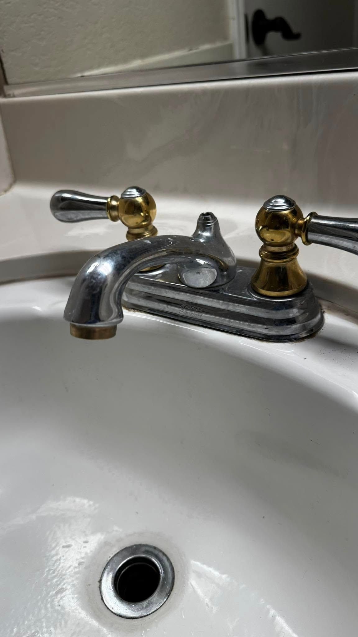 A bathroom sink with a chrome faucet and gold handles.