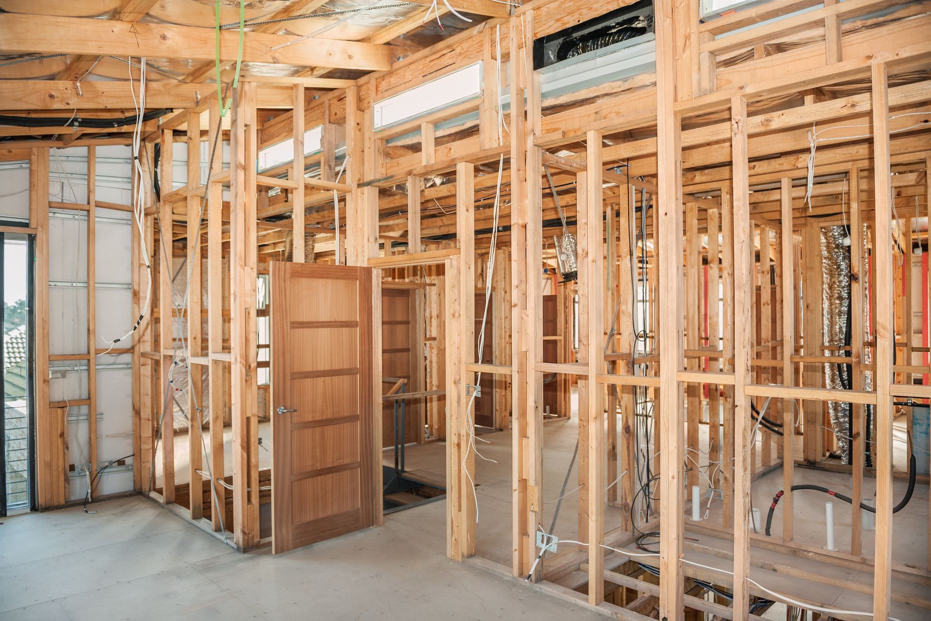 Interior view of a building under construction, wooden framework, door, wires, and concrete floor.