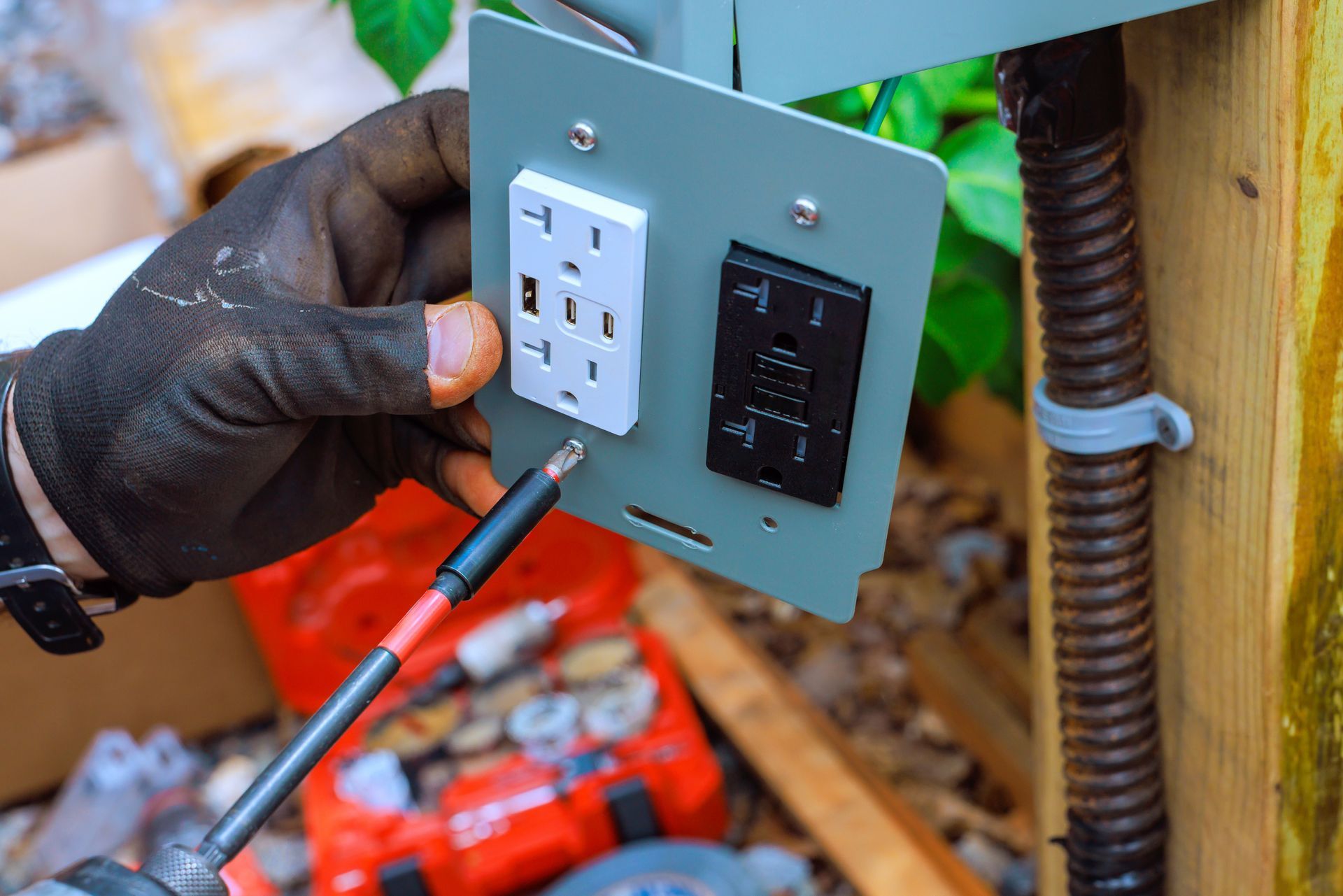 A person wearing a glove installs electrical outlets on a gray panel with a screwdriver.