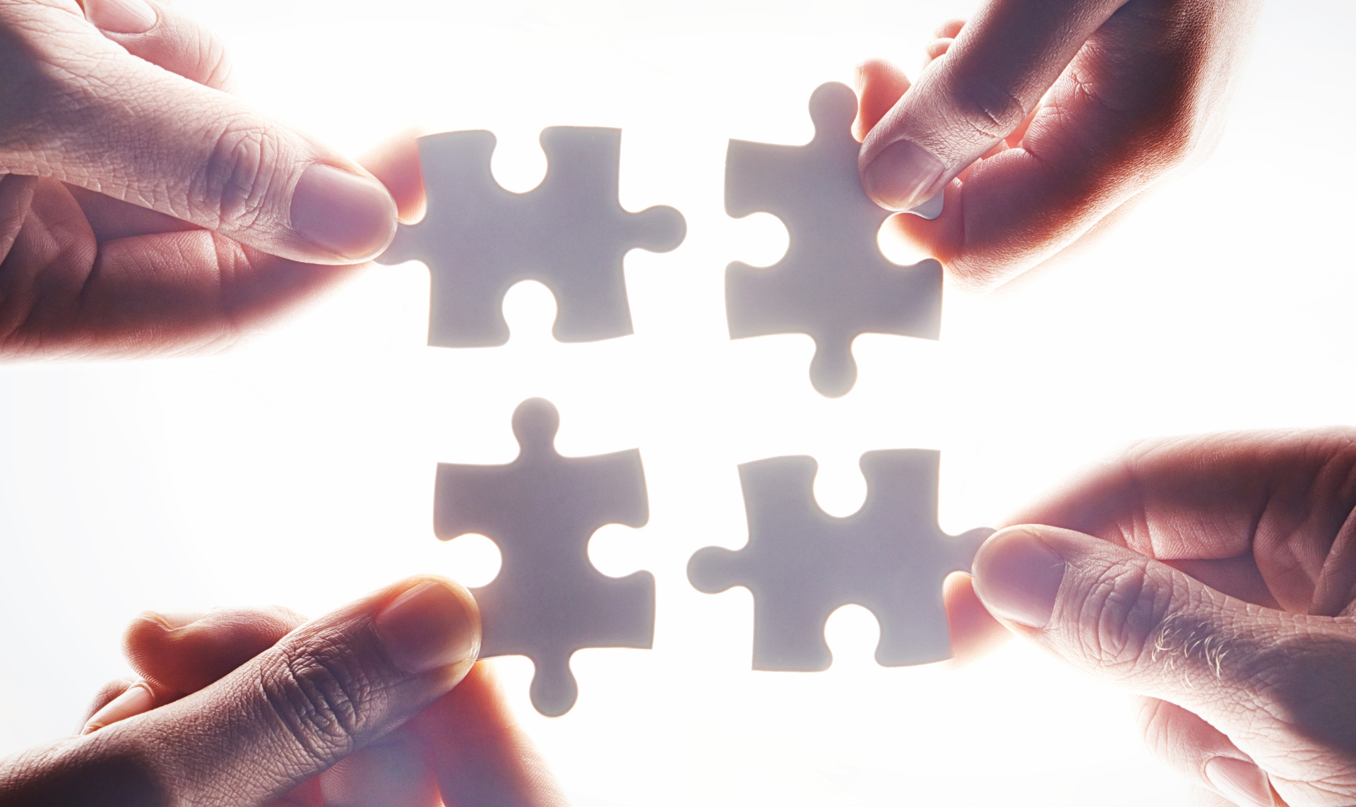 Hands holding puzzle pieces, attempting to connect them to complete a puzzle.