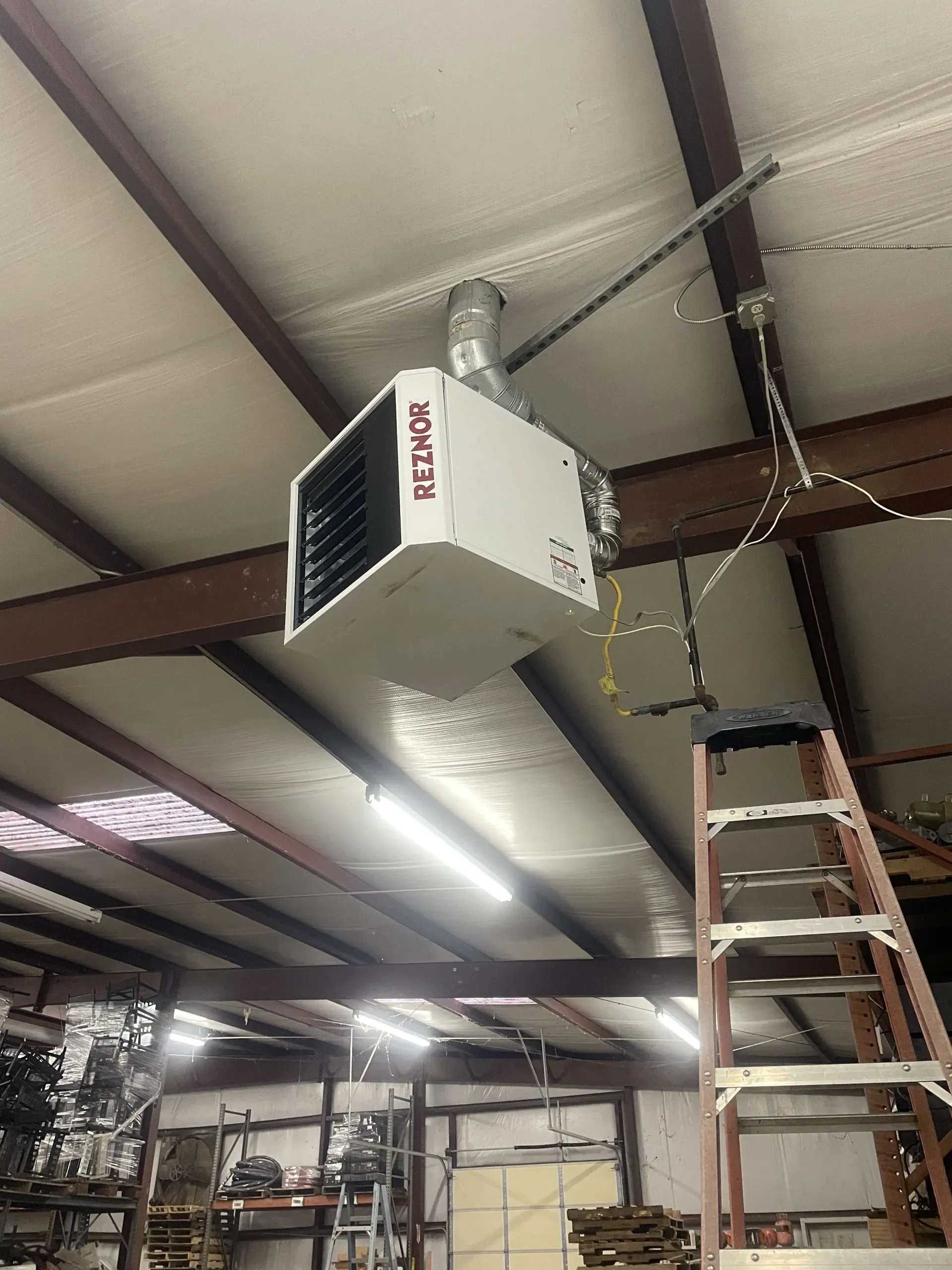 A Reznor unit heater suspended from the ceiling of an industrial building, with a ladder positioned nearby.
