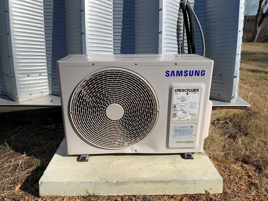 A beige Samsung outdoor air conditioning unit sits on a concrete pad outside a building.