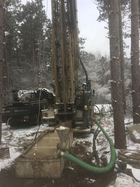 Drilling rig in snowy forest extracting soil. Green hose visible.