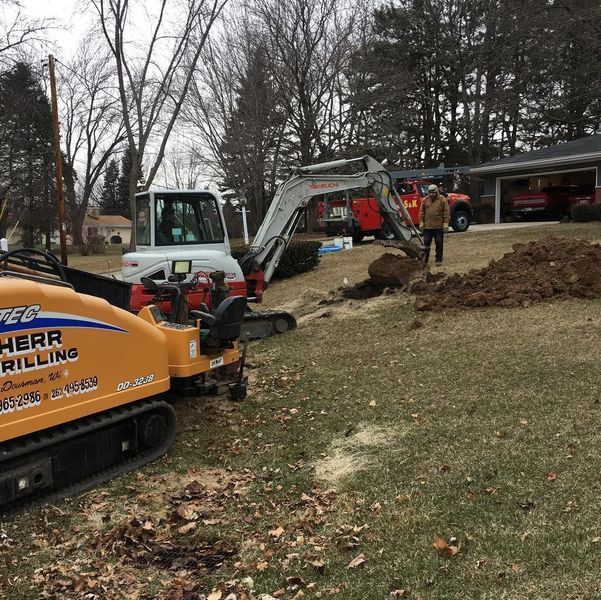 Construction equipment working on a residential property, with an excavator, directional drill, and a worker.