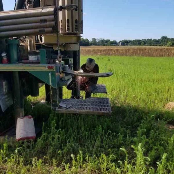 Man welding metal on a drilling rig platform in a grassy field.