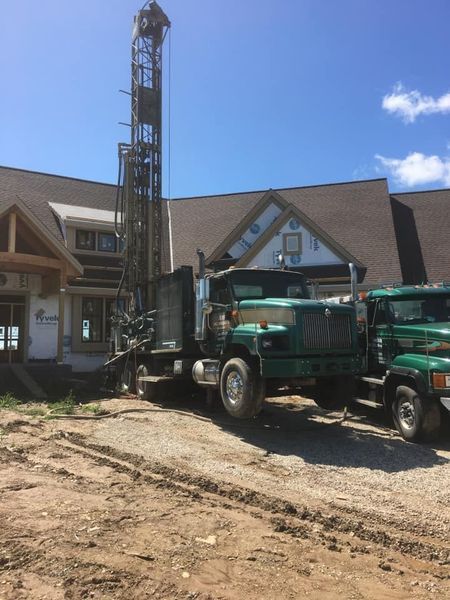 Green drilling truck parked near a house under construction; blue sky.