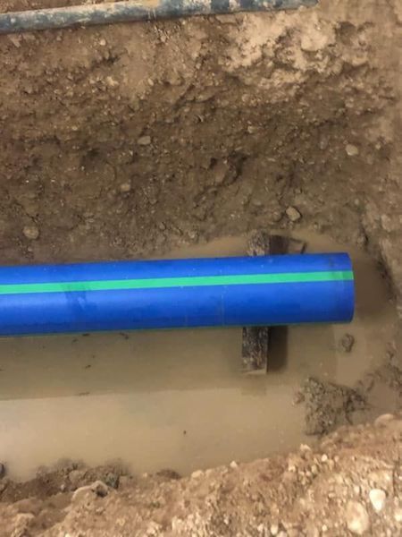 Blue plastic pipe with green stripe in a trench.