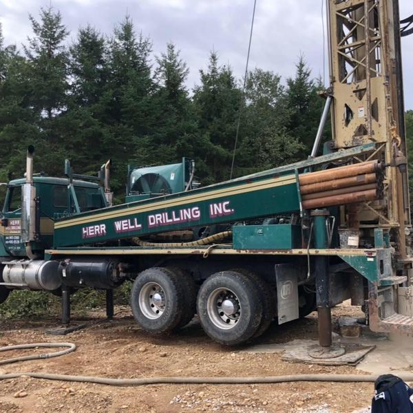 Green Herr Well Drilling truck drilling in a wooded area.