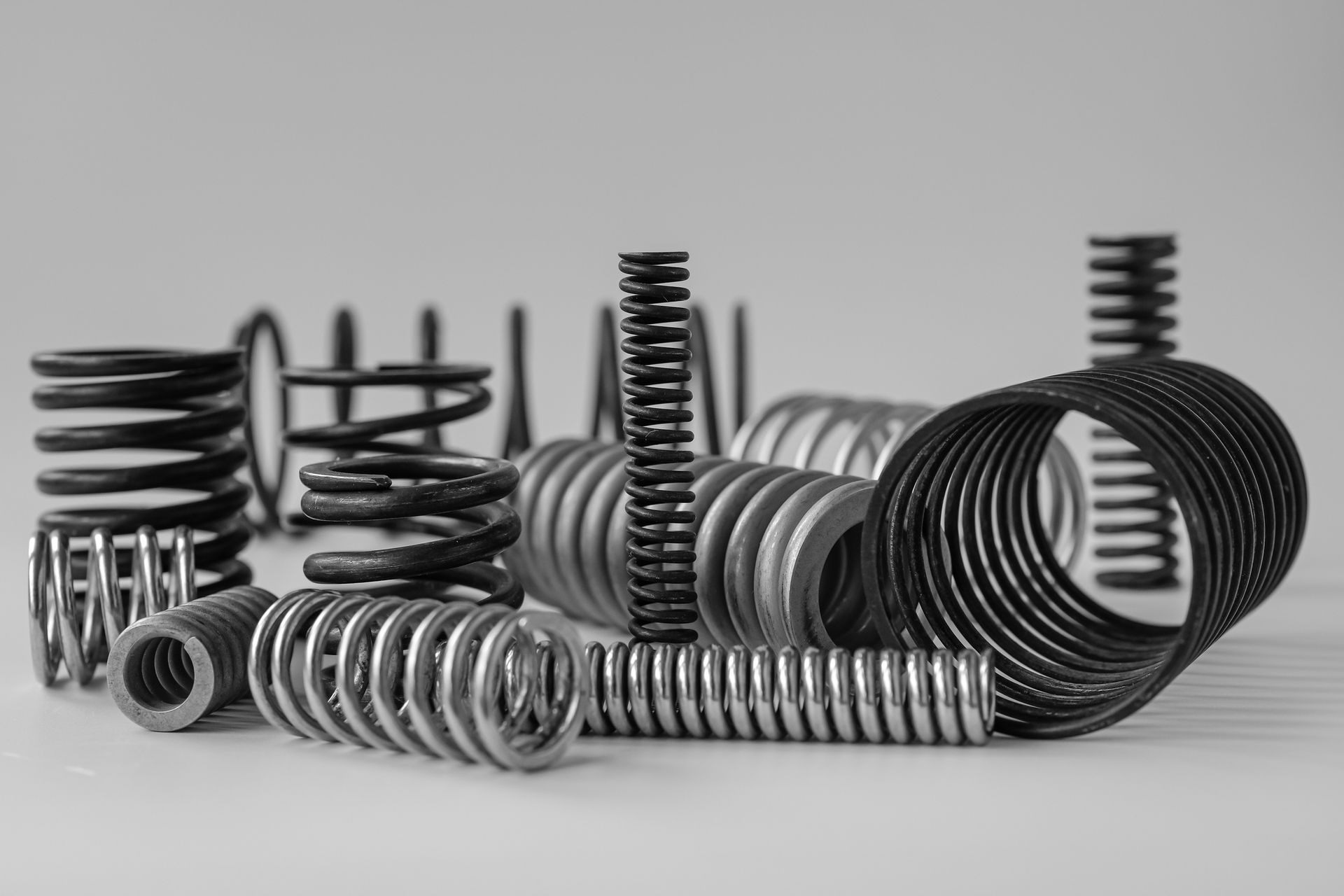 Assorted metal compression springs of different sizes arranged on a plain surface.