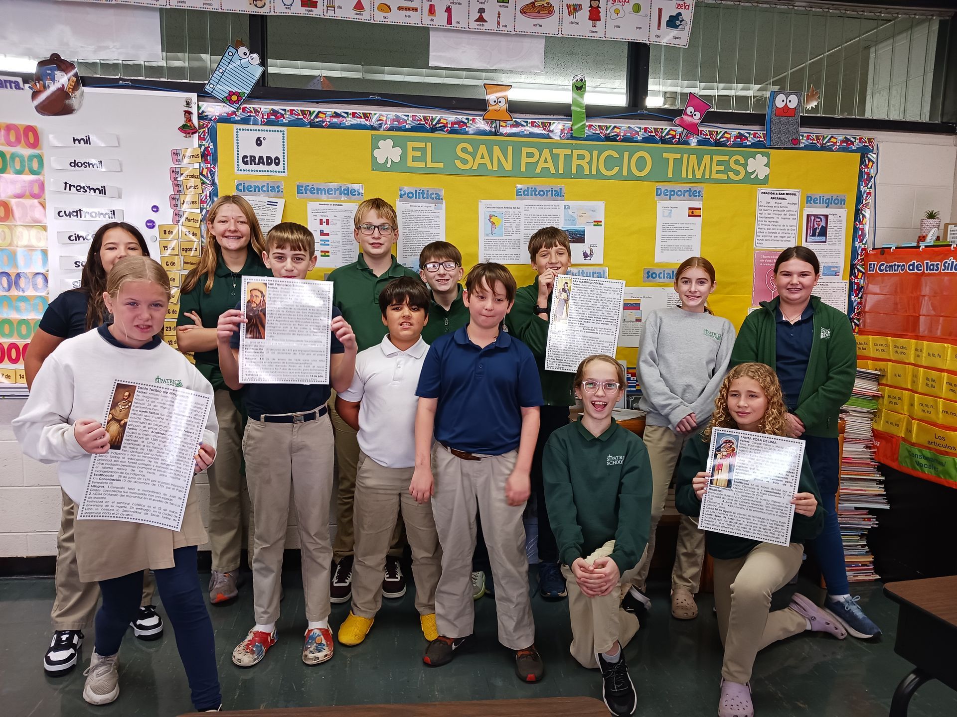 Group of students holding papers in a classroom with bulletin boards.