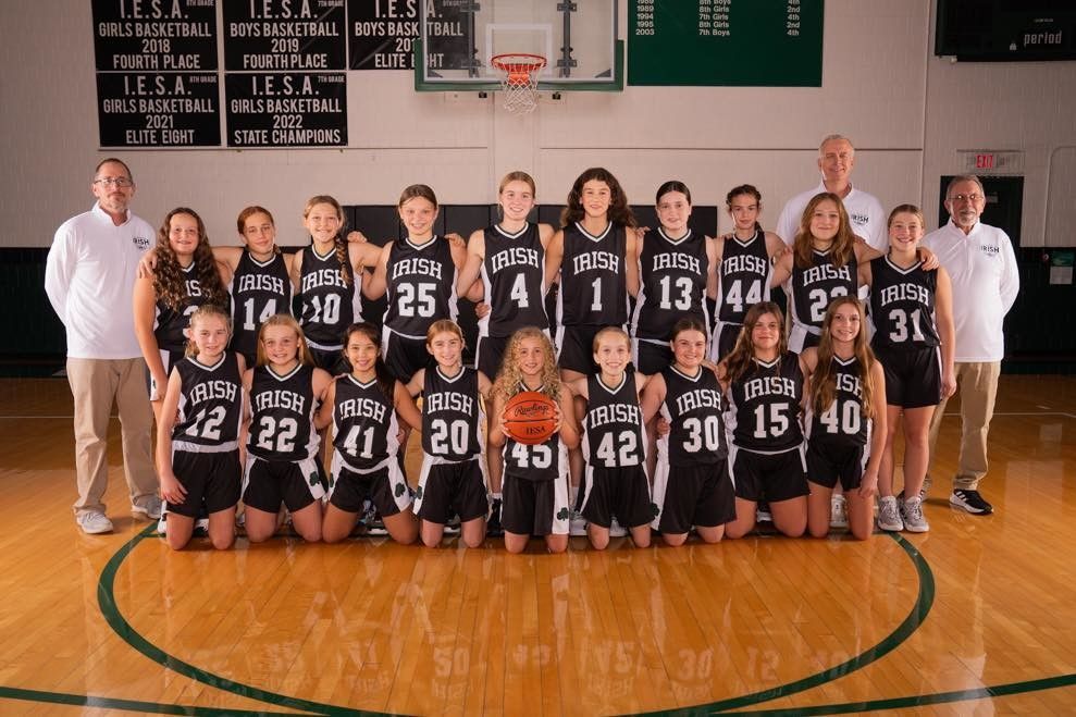 Basketball team photo, girls in black and white uniforms, posing on court, with coaches.