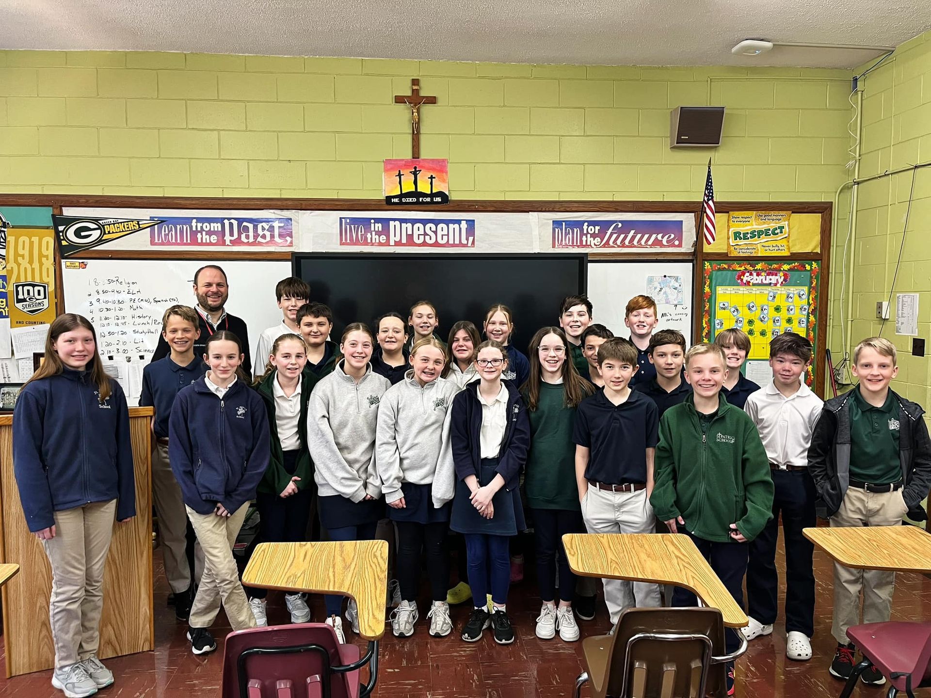 Classroom group portrait; students and teacher, standing in front of a blackboard, classroom setting.