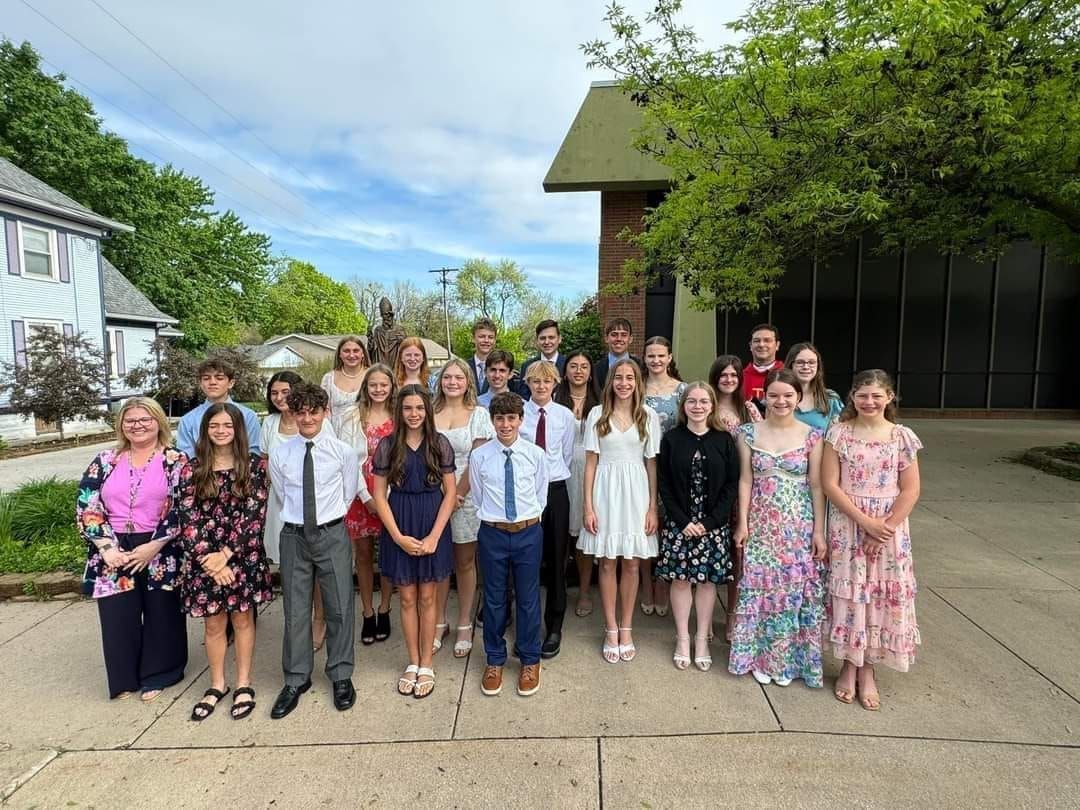 Group of formally dressed young people pose outside a building.