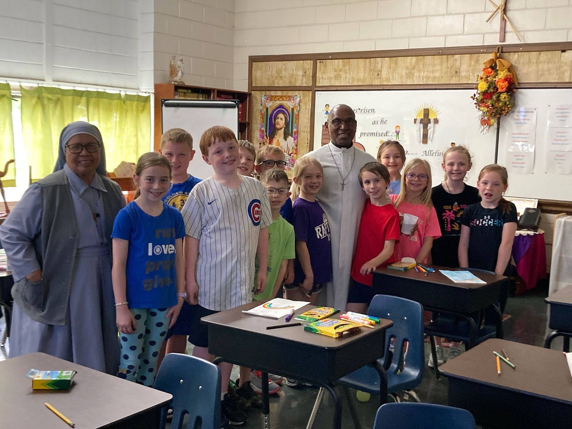 A group of children and adults pose in a classroom; two women and one man standing with them.