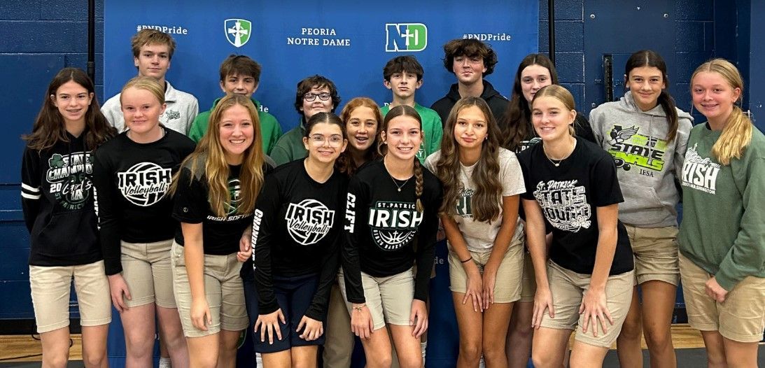Group of students in Irish-themed shirts and khaki shorts posing in front of a blue backdrop.