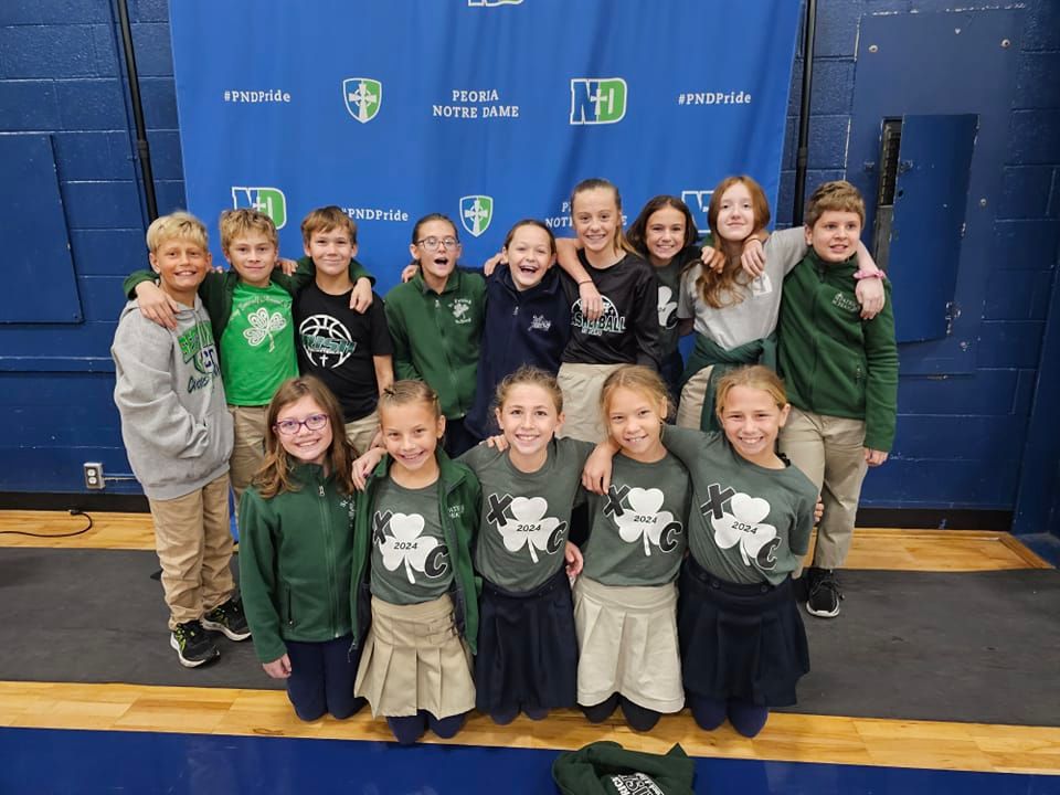 Group of kids smiling and posing in green and tan attire, in front of a blue backdrop.