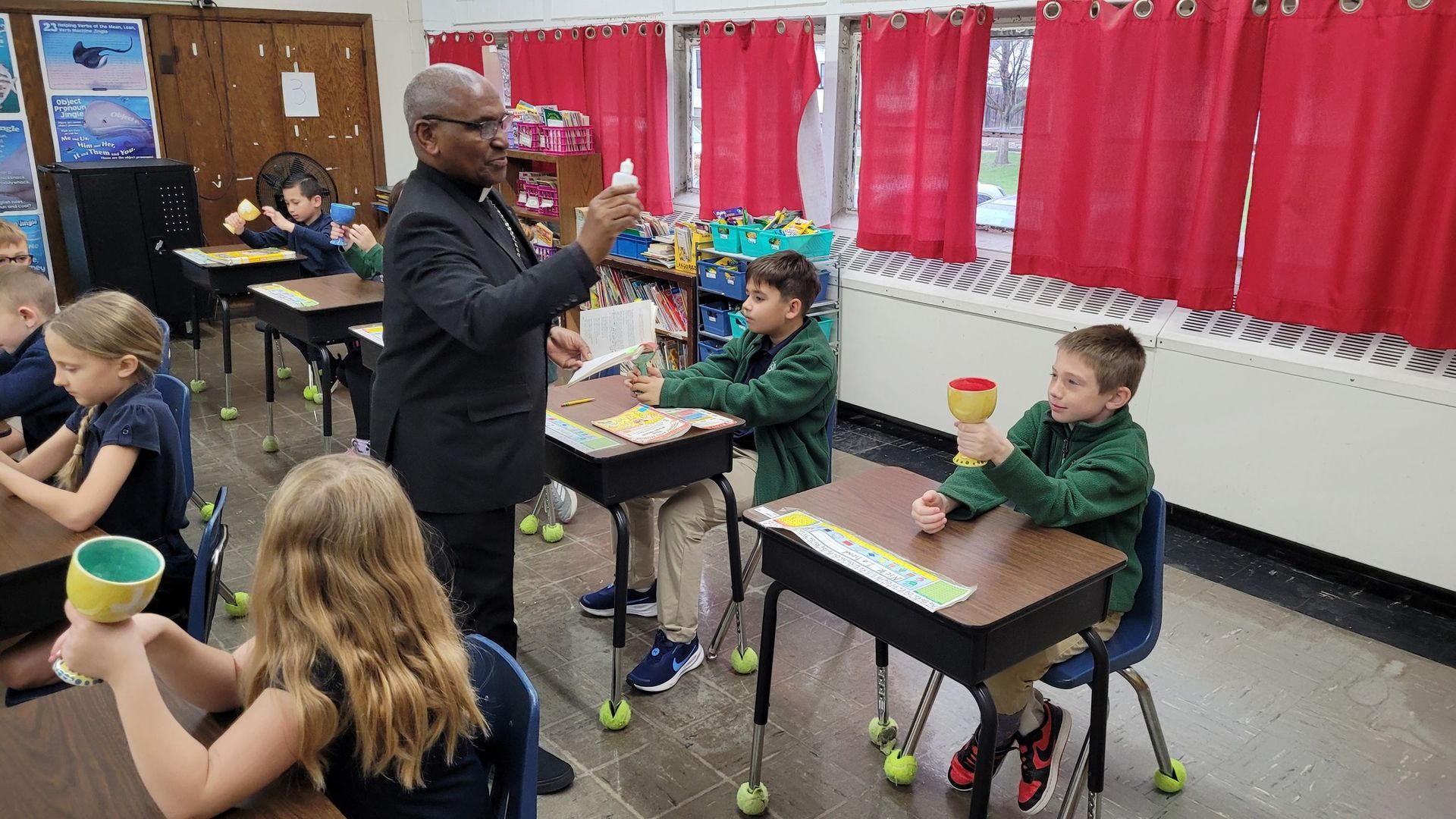 A teacher in a classroom, showing a lesson to students who are holding cups.