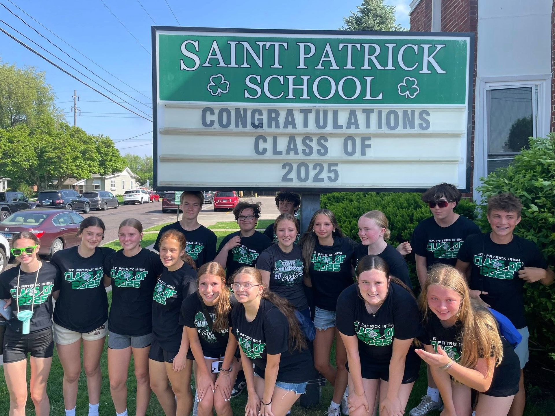 Group of students in black shirts in front of a St. Patrick's School sign, celebrating the Class of 2025.