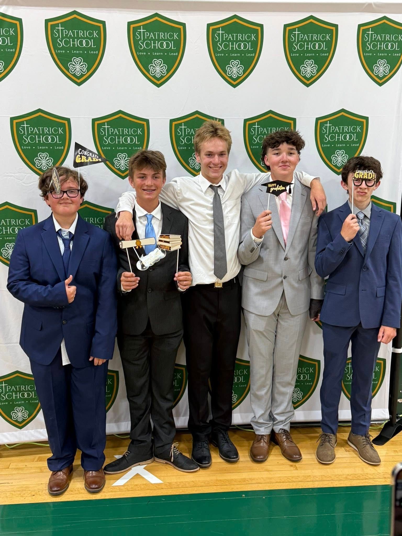 Five young men in suits pose with props in front of a banner.