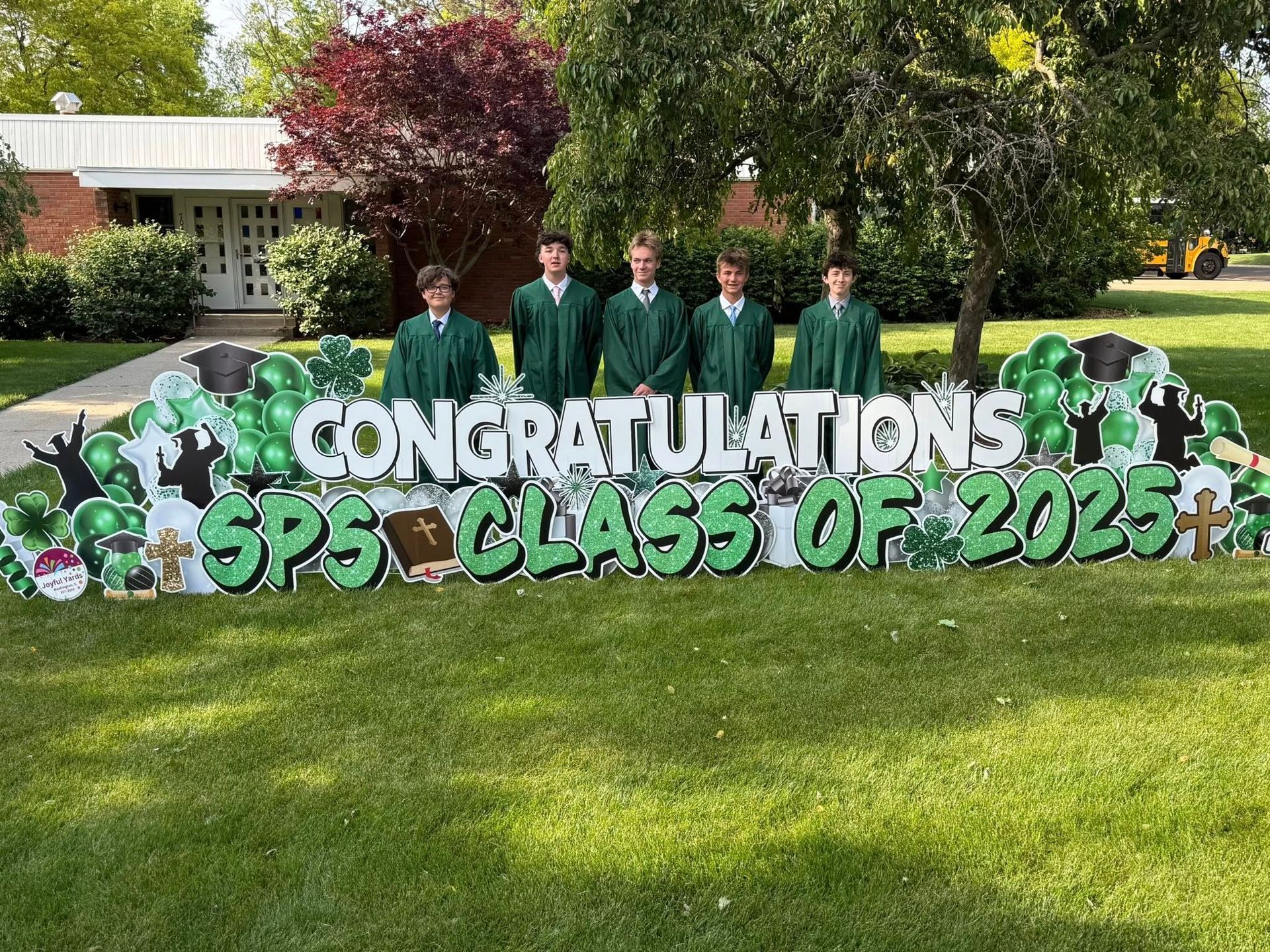 Five young men in green gowns stand behind a 