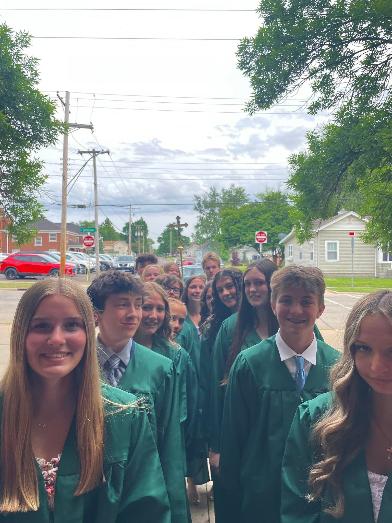 Students in green graduation robes, smiling, lined up outside.