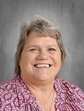 Woman with brown hair and a red floral shirt smiles.