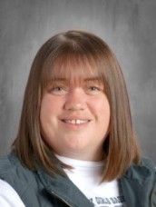 Woman with shoulder-length brown hair and bangs, smiling in a headshot, wearing a blue vest over a white shirt.