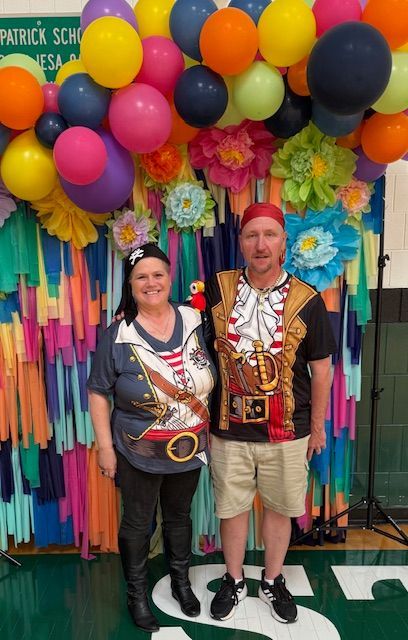 Two people dressed as pirates pose in front of a colorful balloon and crepe paper backdrop.