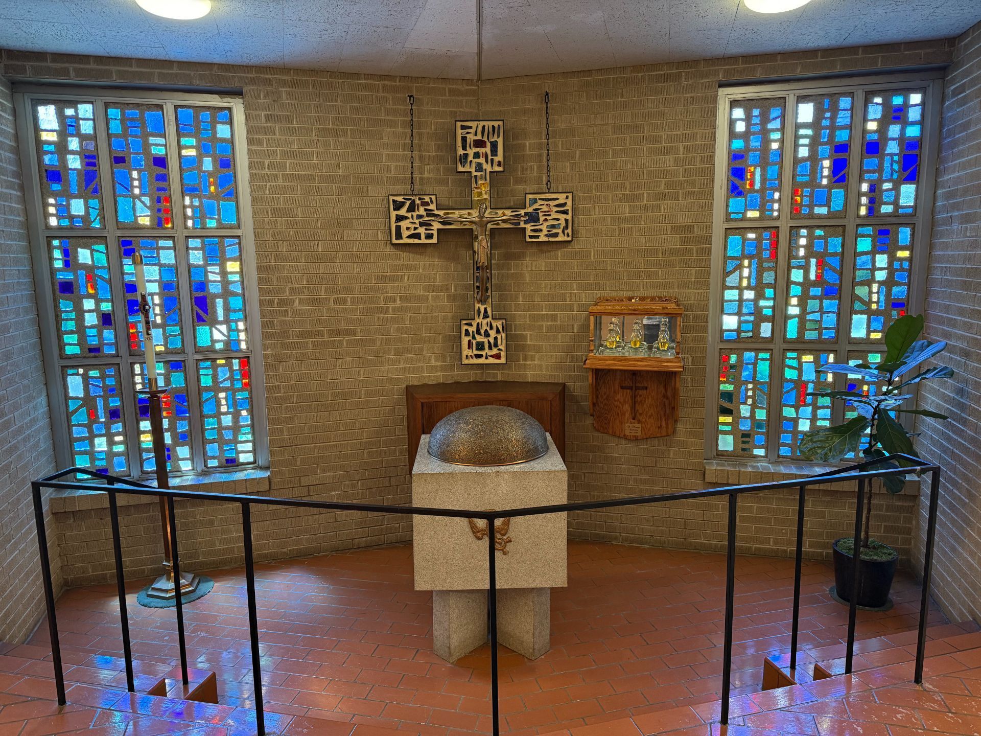 Chapel interior: stained glass windows flank a cross above a stone altar.