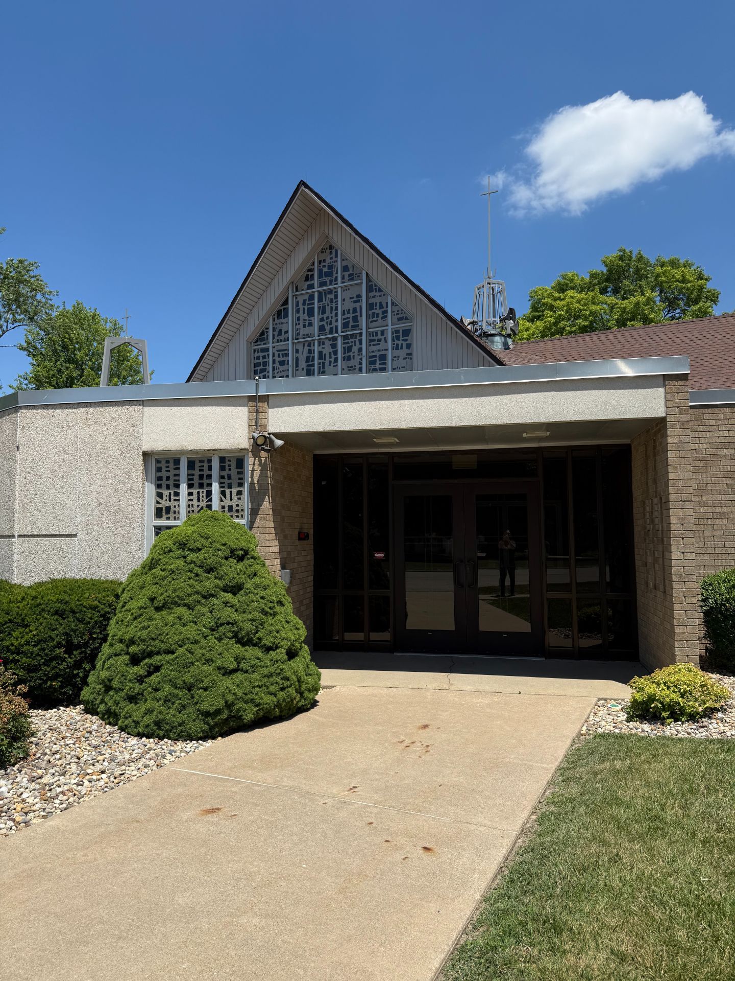 Church entrance with concrete walkway and shrubs. Blue sky overhead.