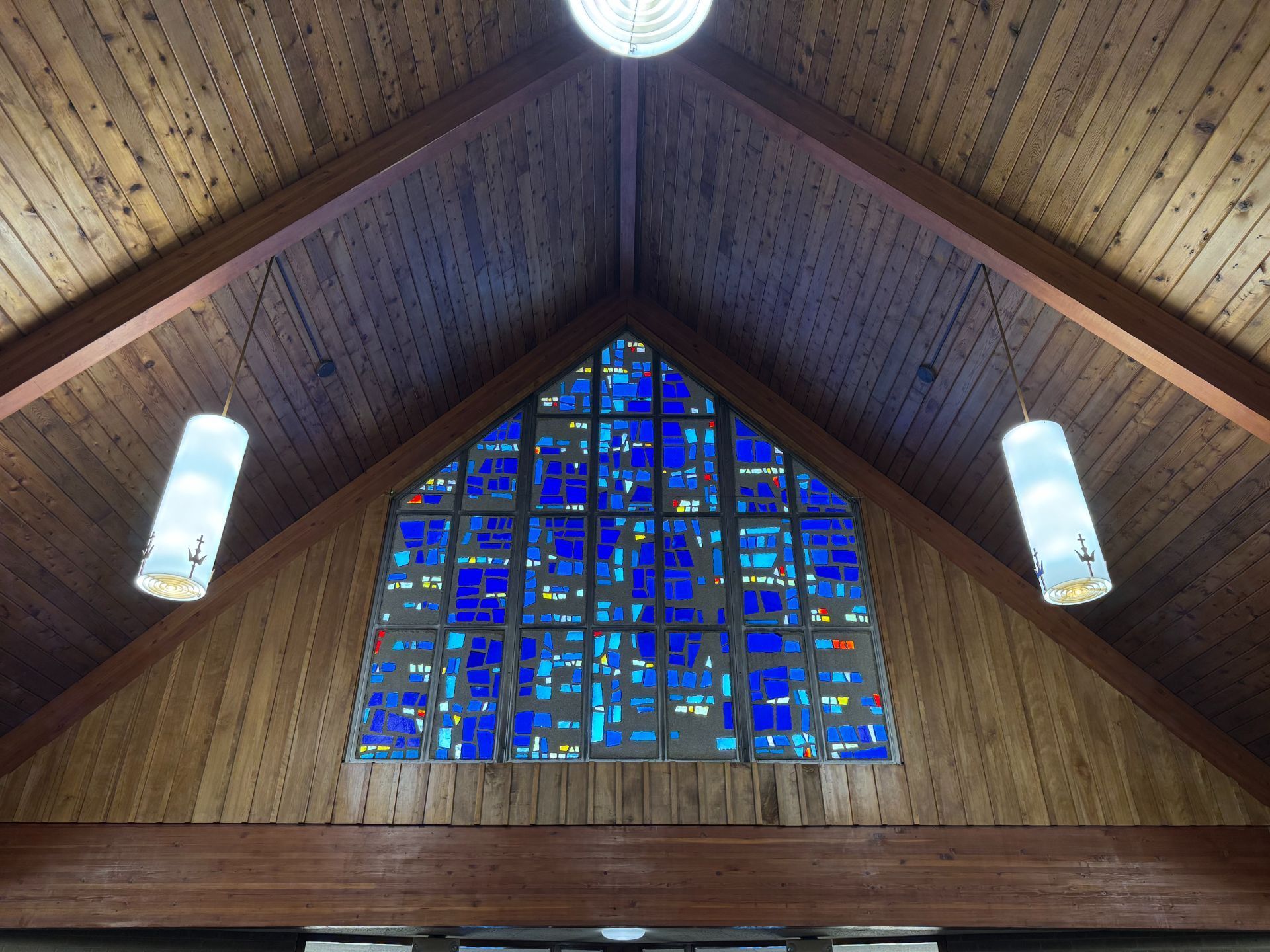 Wooden church interior with a blue stained glass window, two hanging lights.