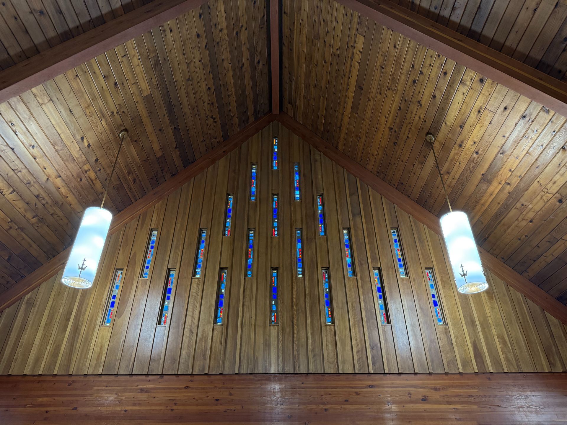 Wooden cathedral ceiling with stained glass windows and hanging lights.
