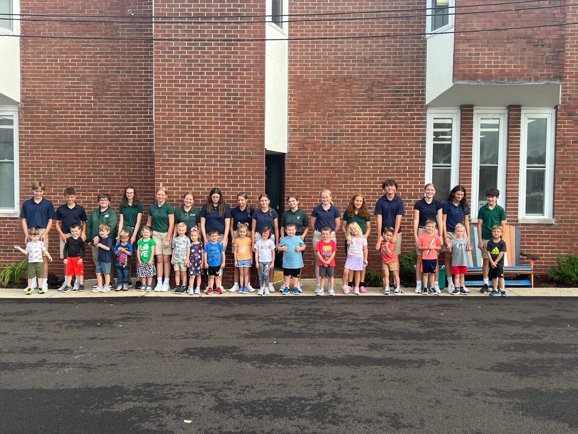 Group photo: Children and adults stand in front of a brick building.