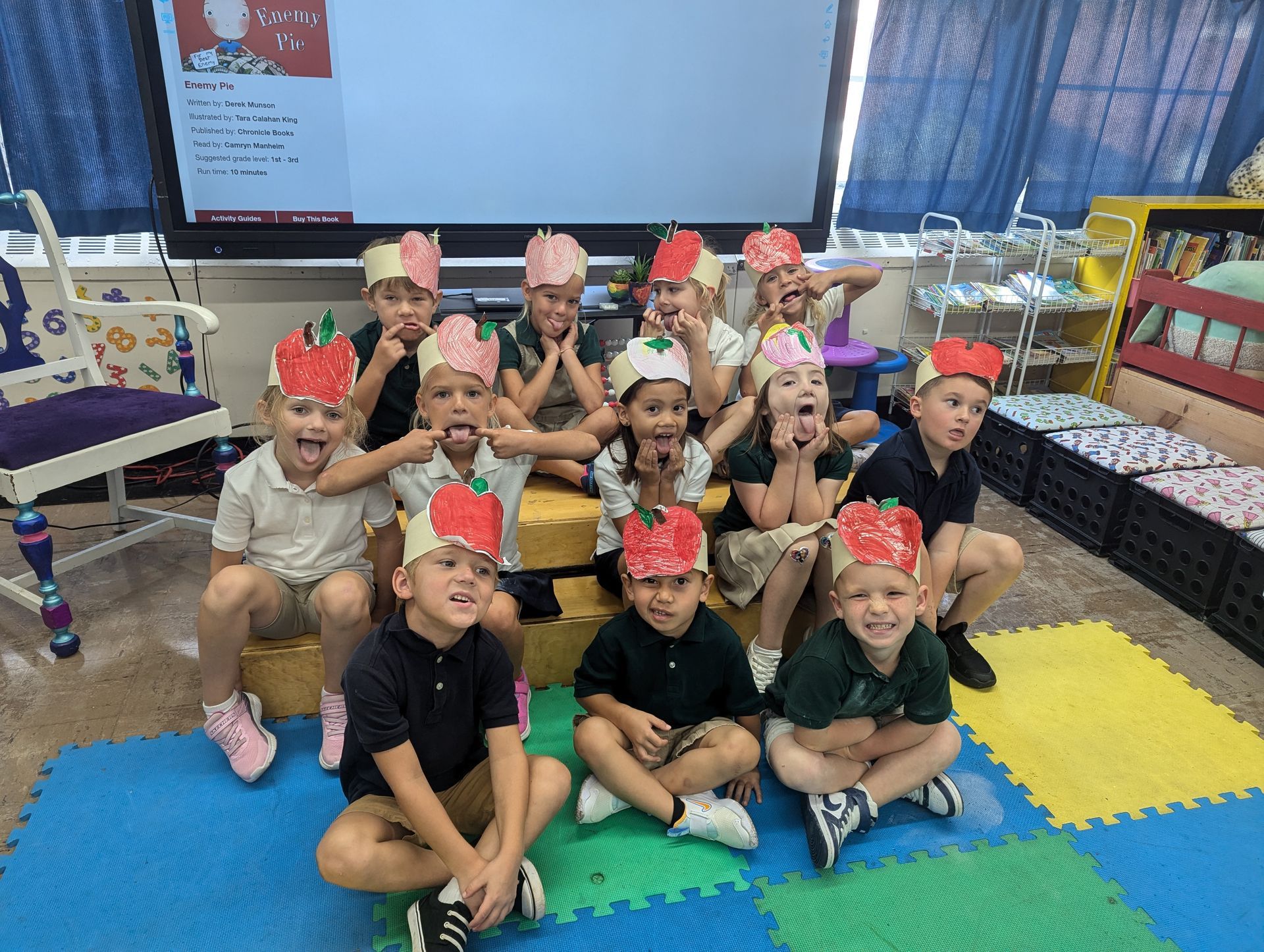 Children in apple hats making silly faces in a classroom.