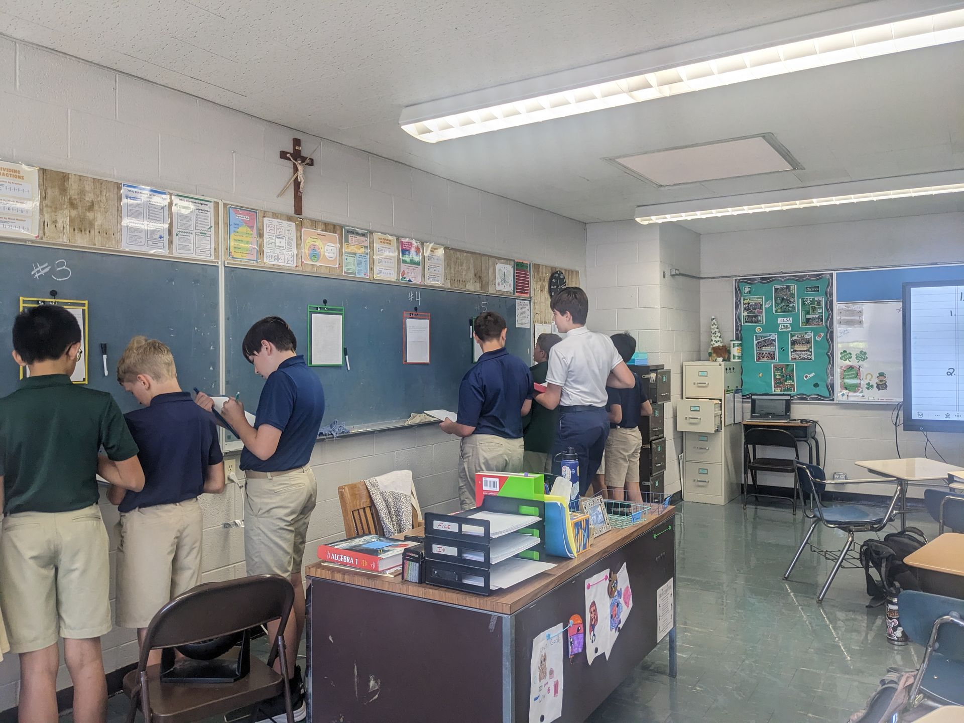 Students in uniform at chalkboard in classroom.