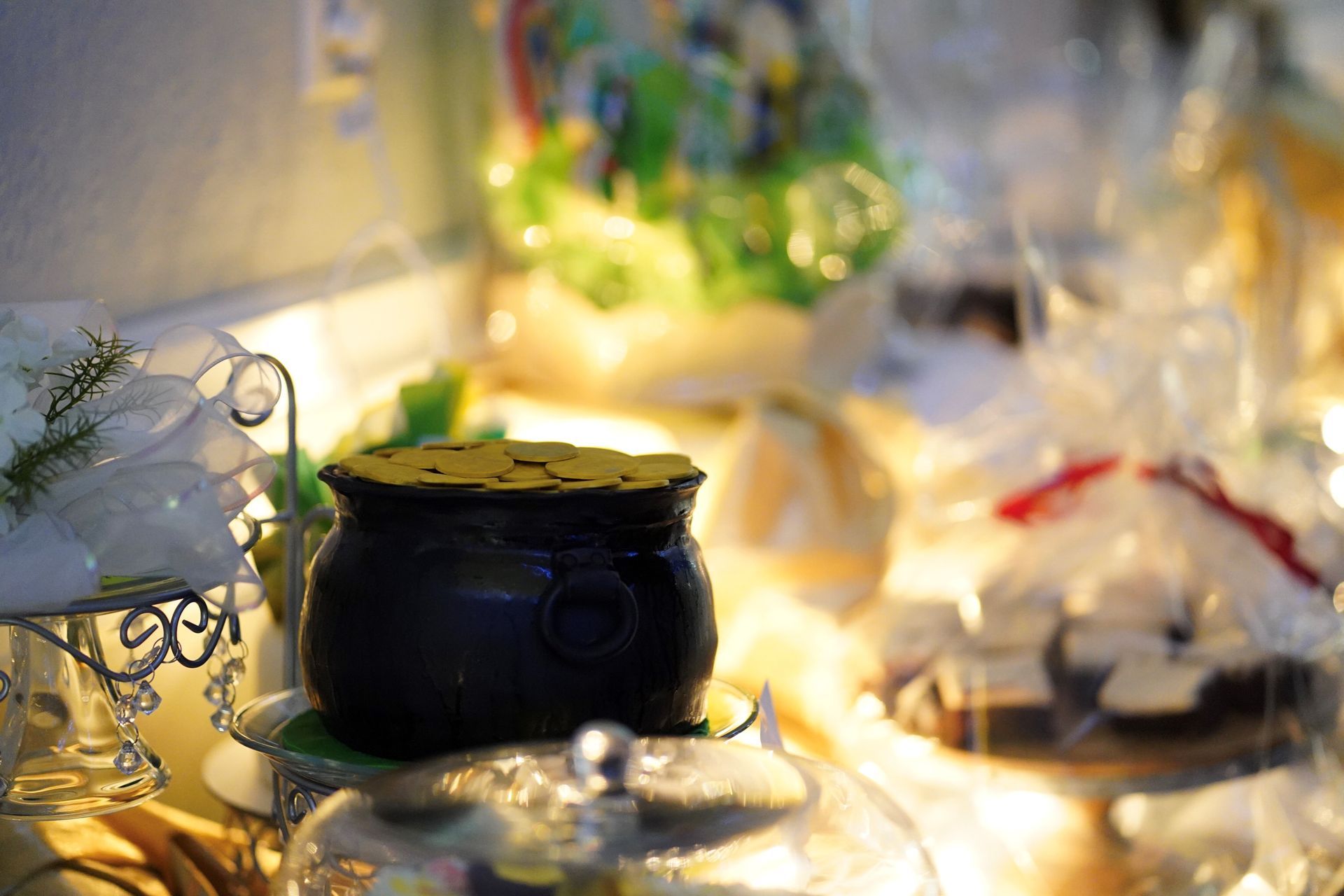 Black pot of gold coins on a silver serving dish, in a display with other wrapped treats.