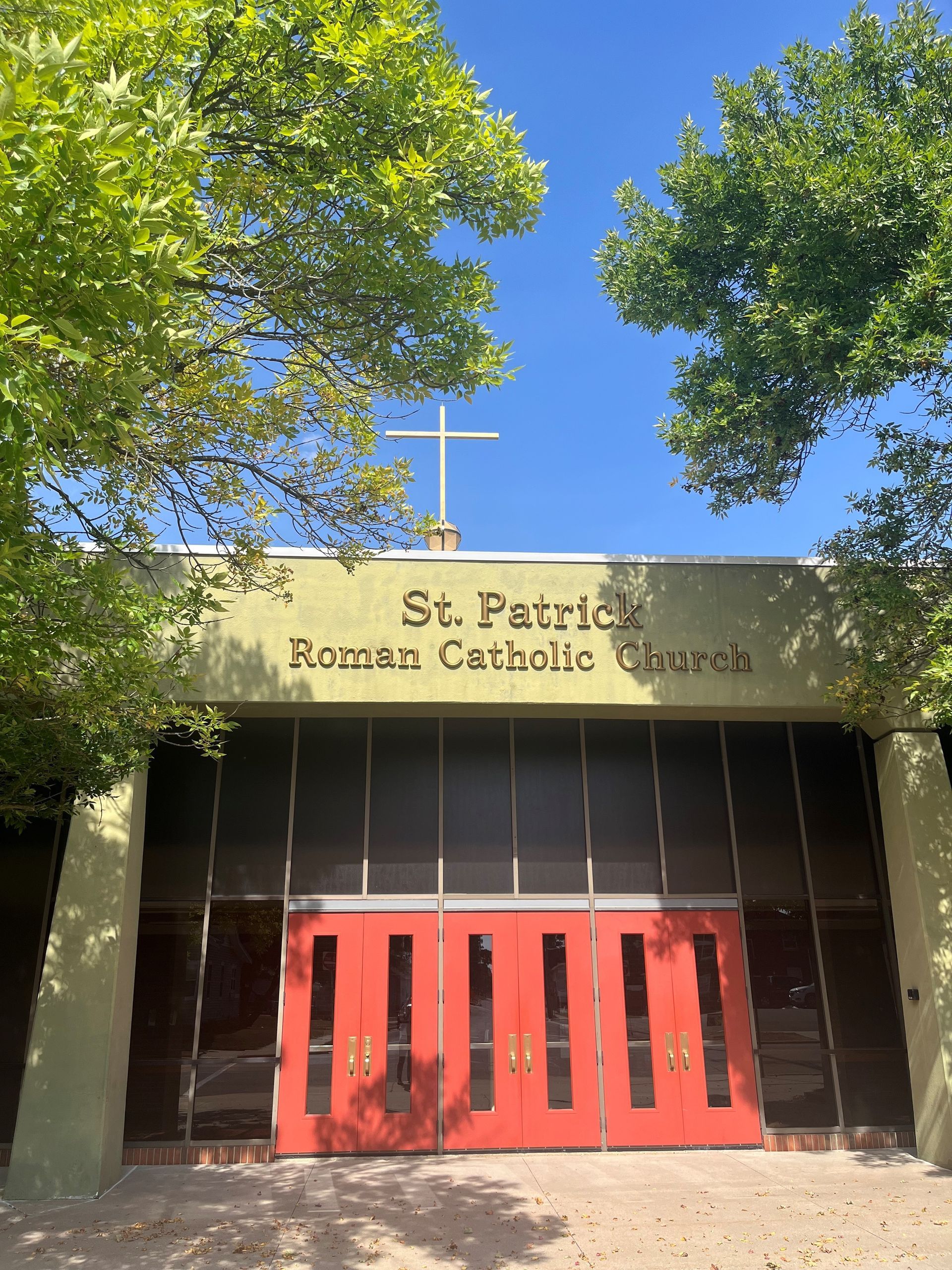 St. Patrick Roman Catholic Church entrance with red doors, a cross, and green trees.