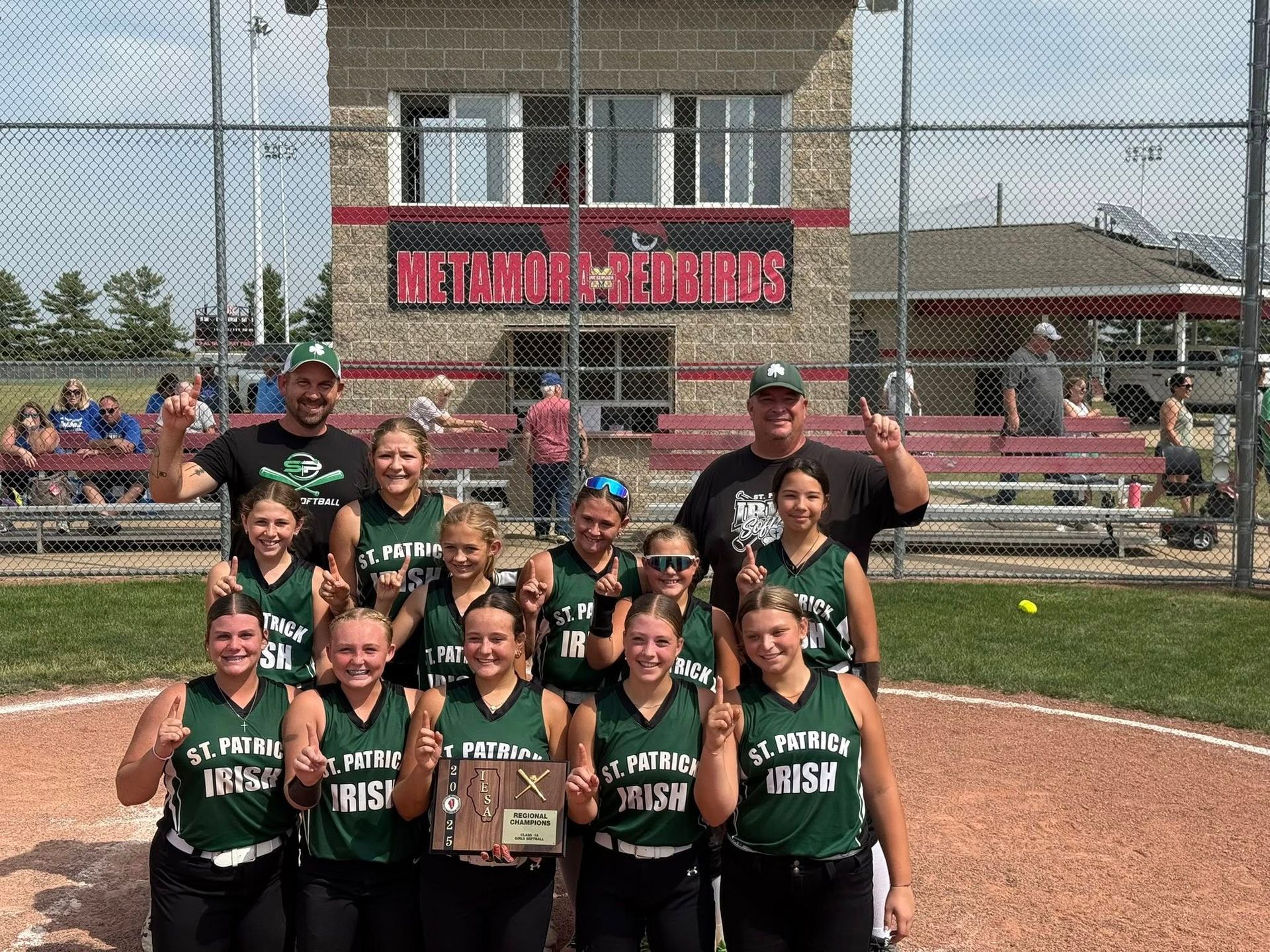 Softball team, St. Thomas Irish, celebrating a win, holding a trophy and posing in front of a building.