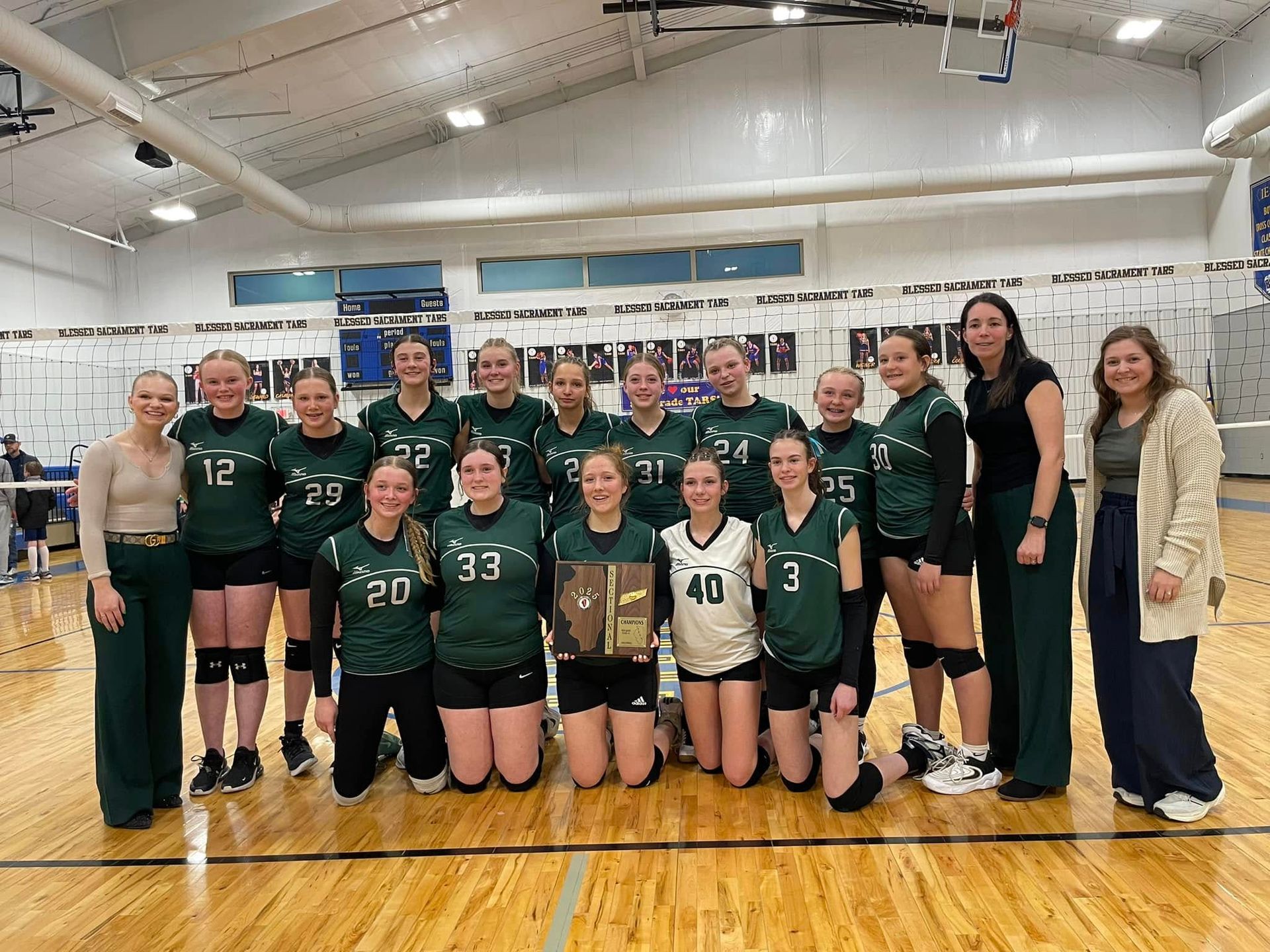 Volleyball team in green jerseys holding a trophy, posing in a gymnasium.