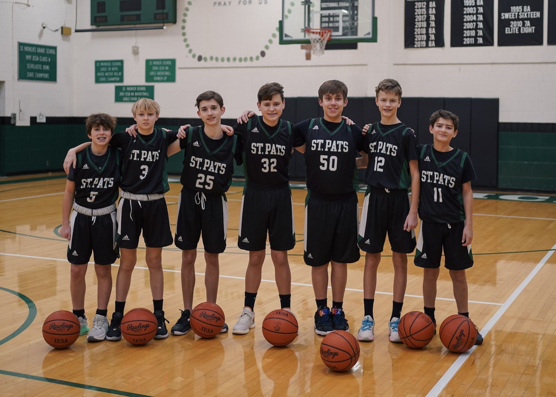 Basketball team of boys in black jerseys with basketballs. Gym setting, smiles.