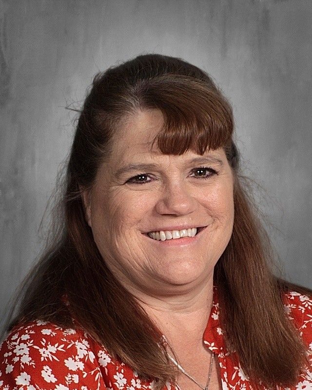 Woman with brown hair and a red floral shirt smiles.