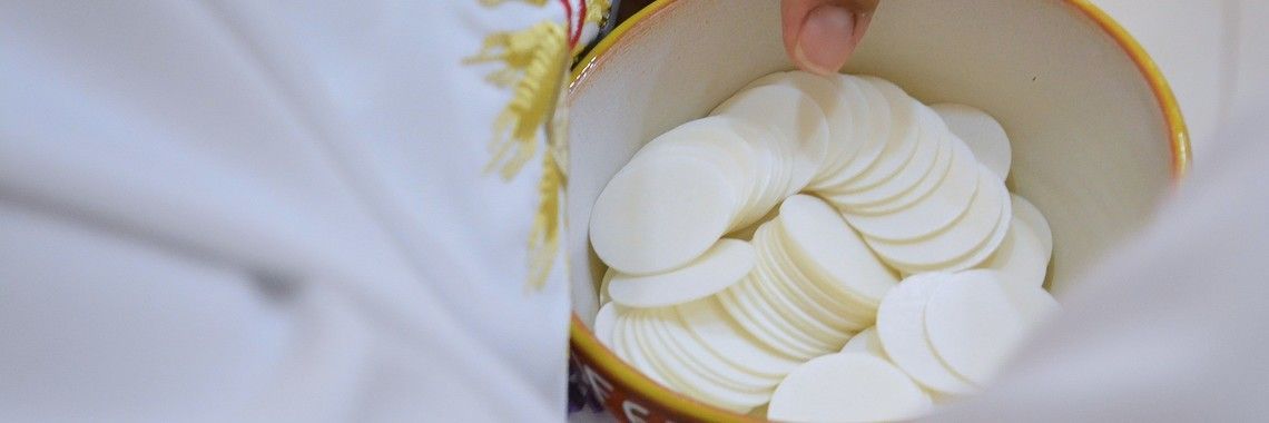 A person holding a bowl of white communion wafers.
