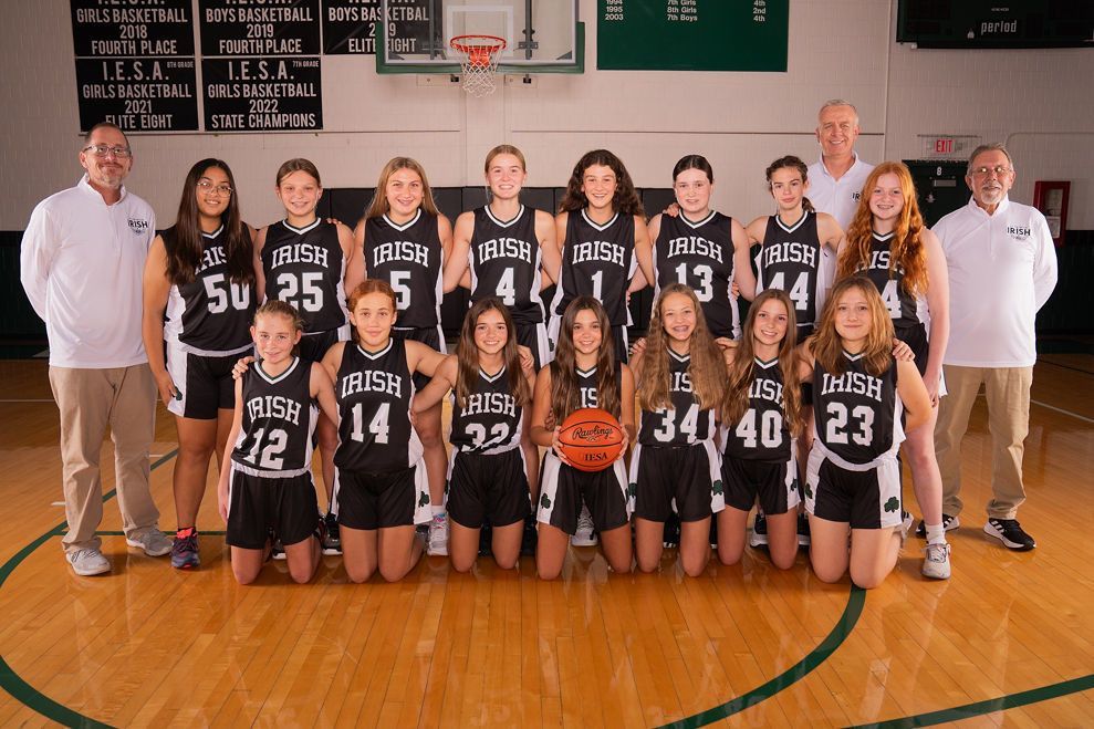 Girls' basketball team in black and white uniforms pose on a wooden court. 