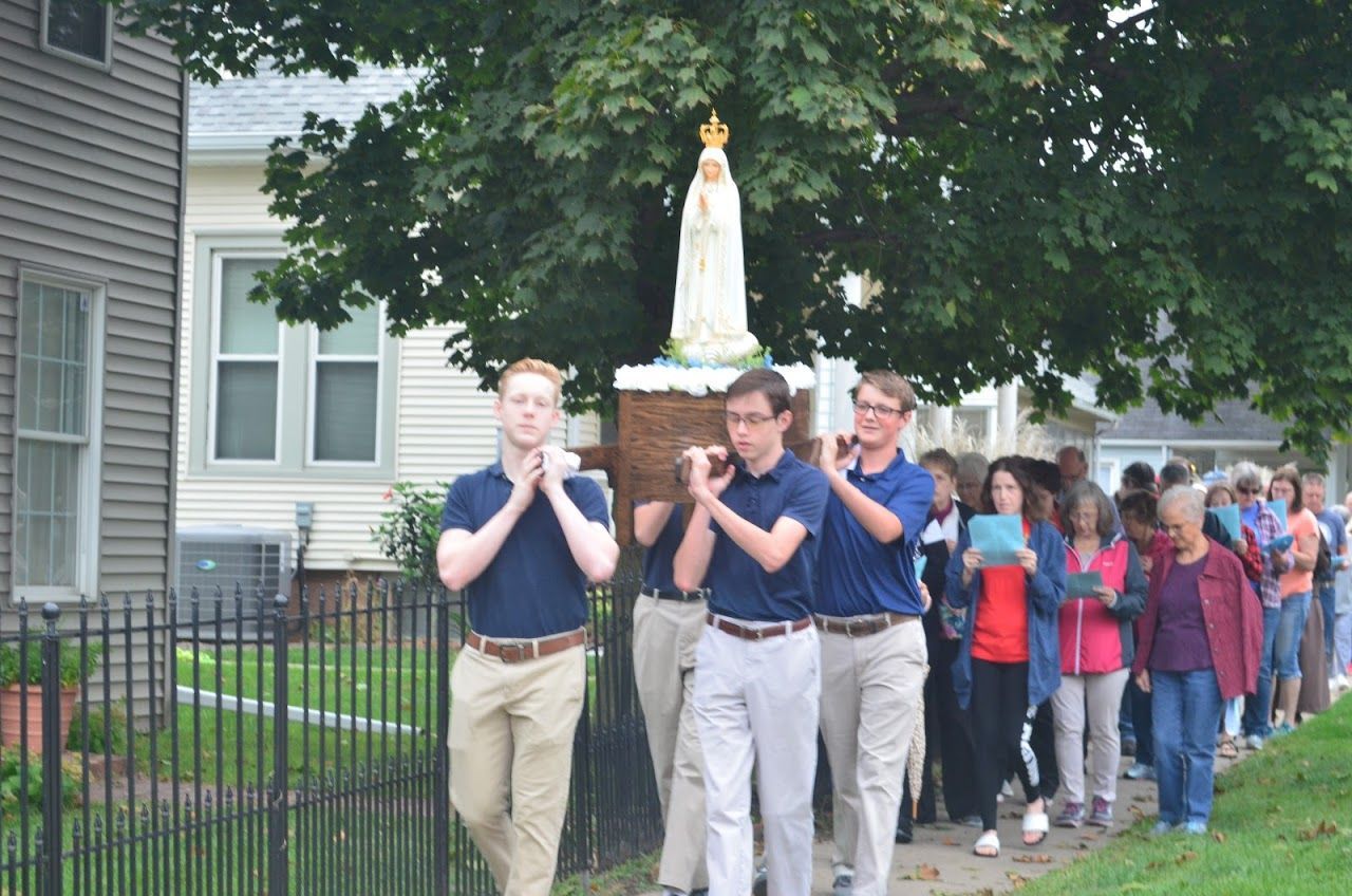 People carrying a statue of the Virgin Mary in a procession down a street.
