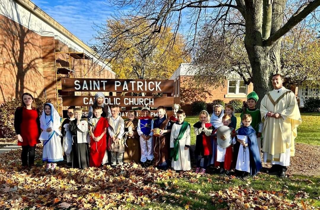 Children in costumes with a priest pose in front of Saint Patrick Catholic Church.