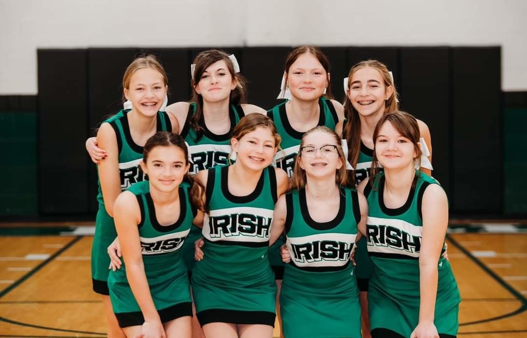 Cheerleaders in green and white uniforms pose in a gym. 