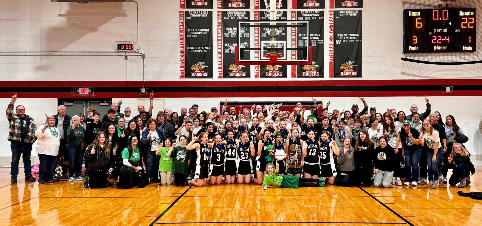Basketball team and fans celebrate on court. Team in uniforms, fans cheering with arms raised in gymnasium.