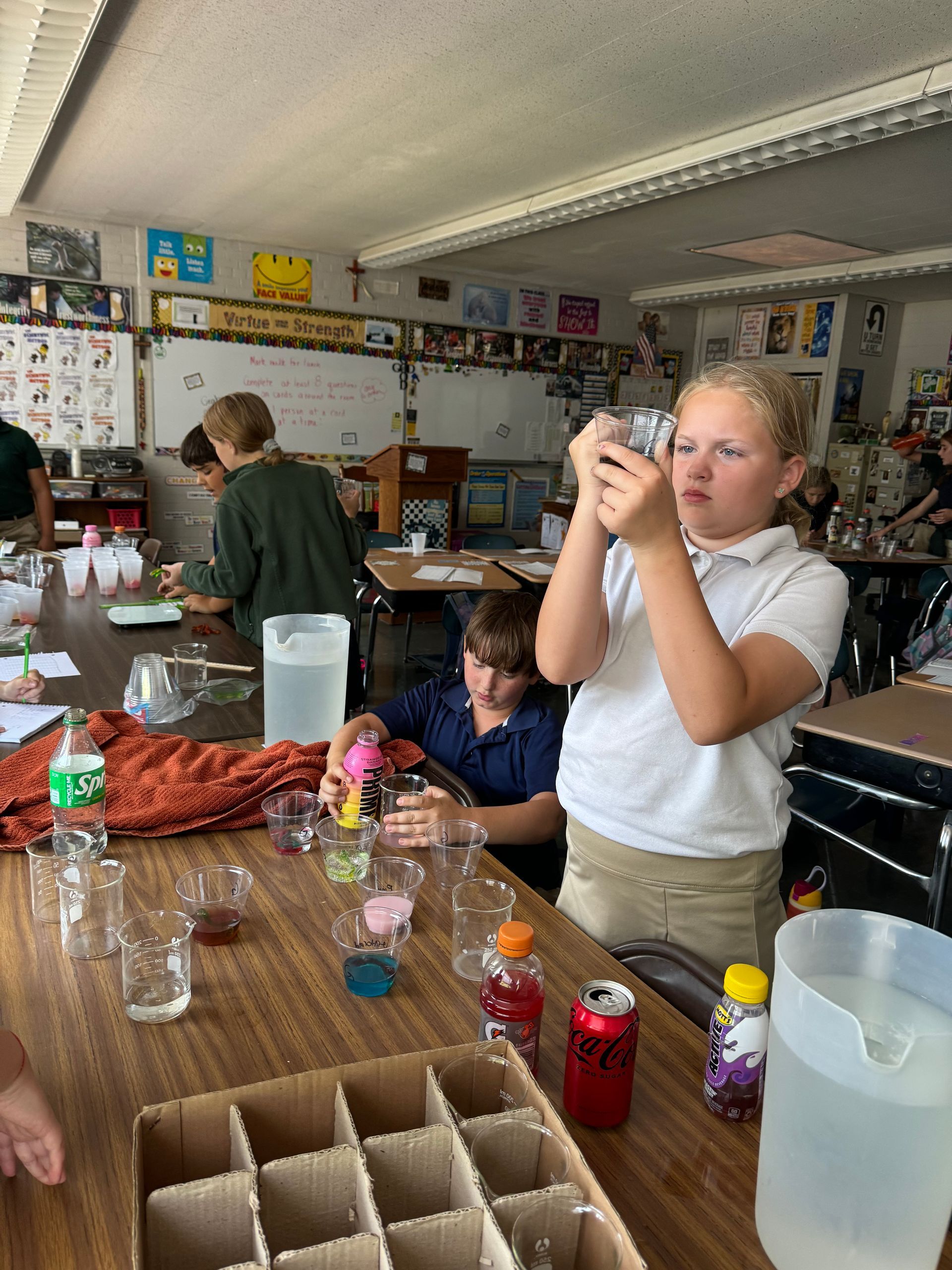 Students in a classroom experiment with liquids in glasses. One girl examines a glass.